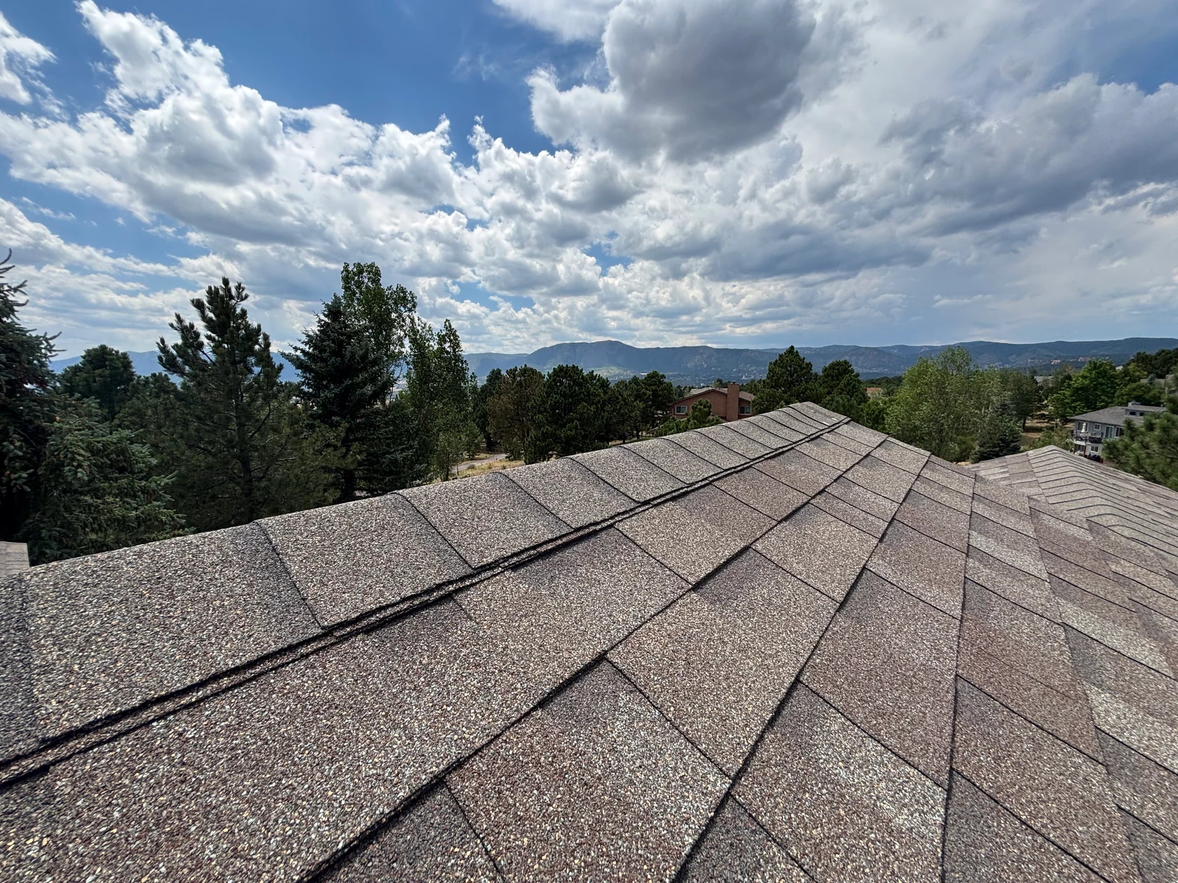 Shingle roof ridge with trees and mountains beyond in Colorado Springs